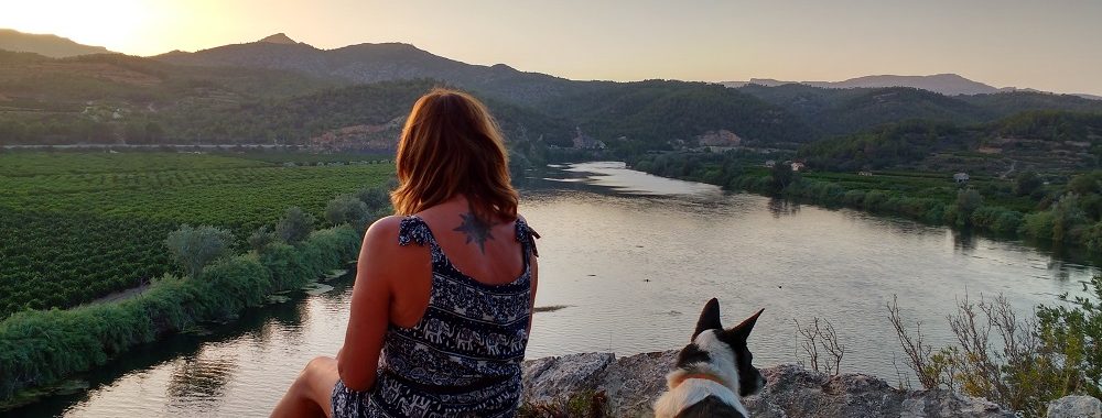 Jane Clements and dog looking out over a river at sunset